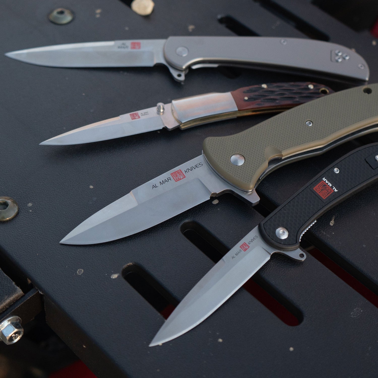 A collection of Al Mar Knives on a black metal surface