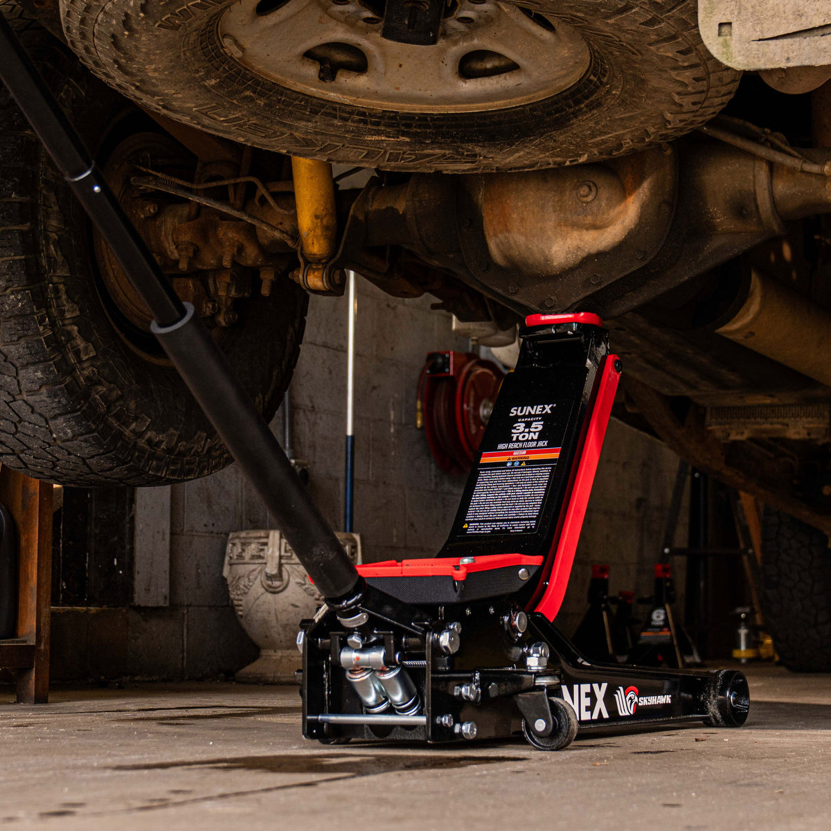 The SUNEX SKYHAWK Floor Jack being used to lift a heavy-duty diesel truck.