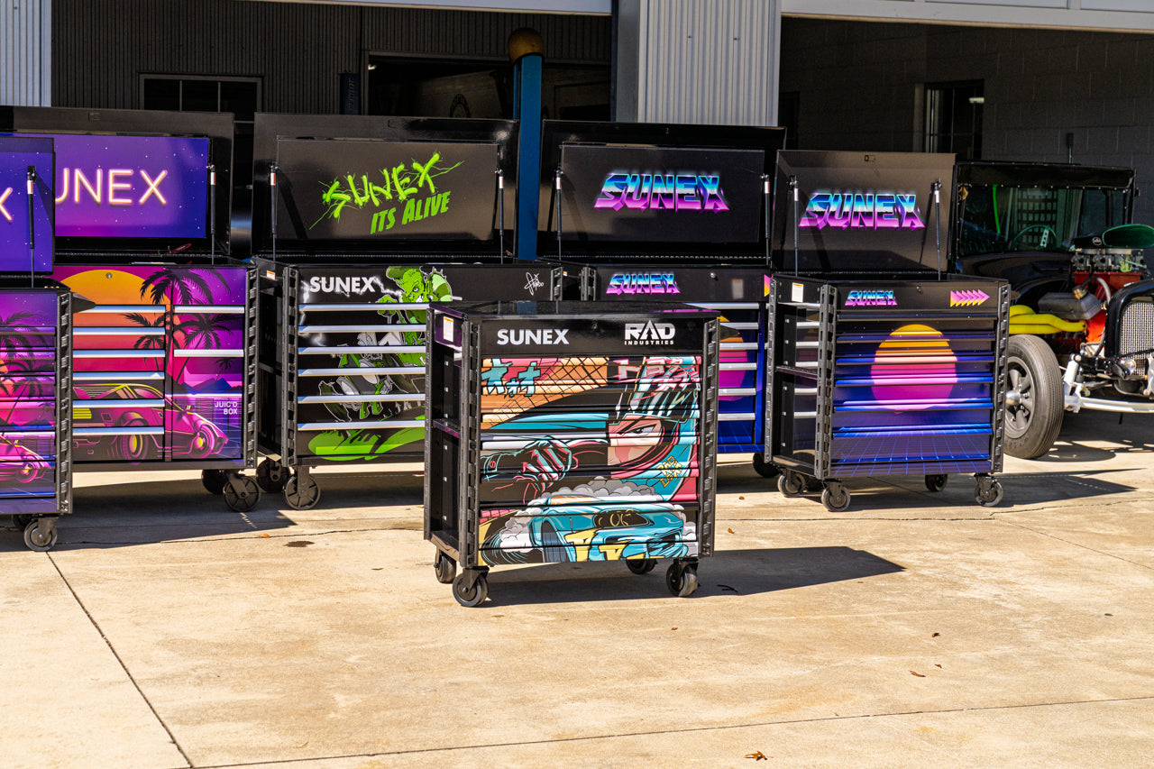 Colorful themed service carts with SUNEX branding in front of service bays with classic cars in the background.